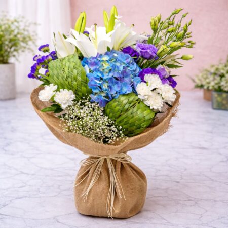 Blue hydrangea bouquet with white lilies, carnations and woven leaf detailing wrapped in jute by FreshKnots Bangalore with same day delivery.