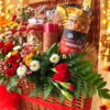 Gourmax Lime Chilli Makhana Bhel jar, scented pillar candle and dry fruit jars in a wicker hamper with red carnations, side view