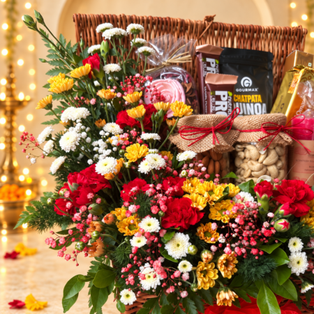 Close-up of red spray carnations, yellow and white santini, Calimero chrysanthemums and pink baby's breath in a wicker hamper with almond and cashew jars