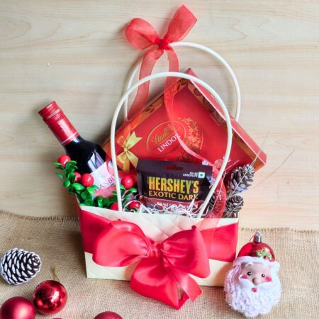 Christmas-themed gift bag with wine, Lindt chocolates, Hershey’s dark chocolate, pinecones, and red ribbon.