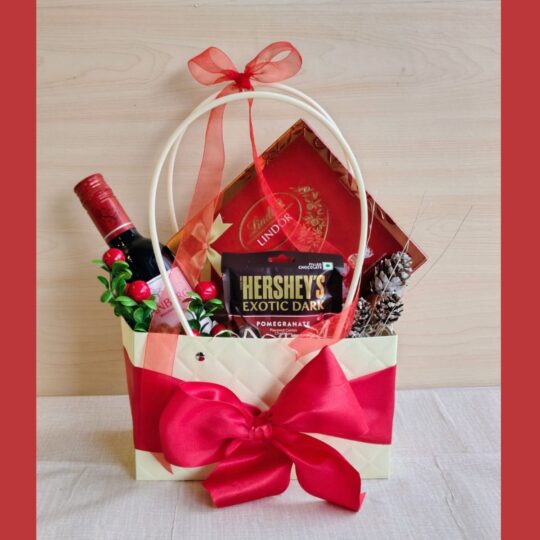 Christmas-themed gift bag with wine, Lindt chocolates, Hershey’s dark chocolate, pinecones, and red ribbon.