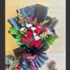 Christmas-themed bouquet with red carnations, white flowers, greens, and gold accents in black wrapping.