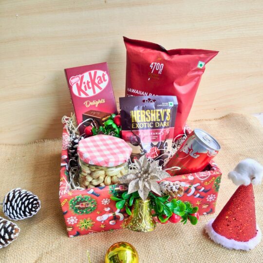 Christmas treat hamper with chocolates, popcorn, nuts, beverage can and festive décor placed in a red Christmas box.