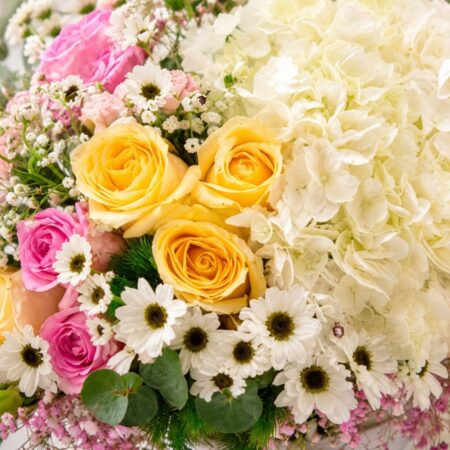 A pastel floral arrangement in a glass vase featuring white hydrangeas, yellow and pink roses, white daisies, and pink fillers, tied with a white ribbon, ideal for same day flower delivery in Bangalore