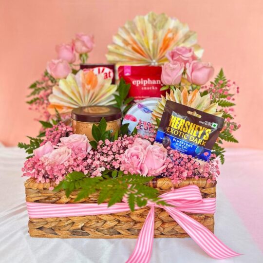 Gift hamper with chocolates, pink roses, baby’s breath, and a candle arranged in a woven basket with a pink ribbon