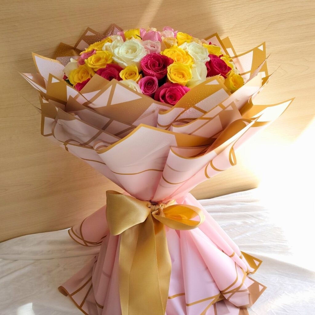 A vibrant mixed rose bouquet with pink, yellow, and white roses, elegantly wrapped in blush and gold paper with a satin bow — available for same day flower delivery in Bangalore.