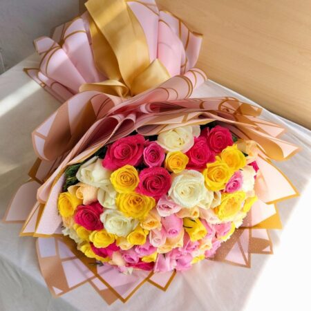 A vibrant mixed rose bouquet with pink, yellow, and white roses, elegantly wrapped in blush and gold paper with a satin bow — available for same day flower delivery in Bangalore.