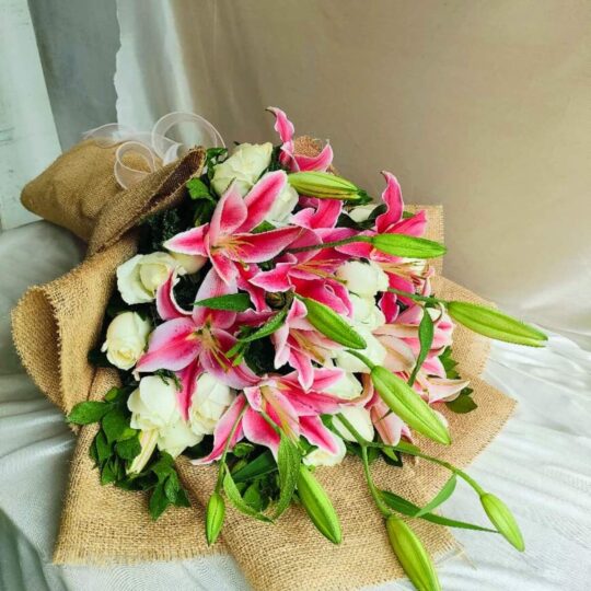 Fresh lily and rose bouquet wrapped in burlap, featuring pink lilies, white roses, and lush green buds.