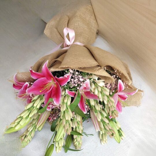 Fresh lily and rose bouquet wrapped in burlap, featuring pink lilies, white roses, and lush green buds.