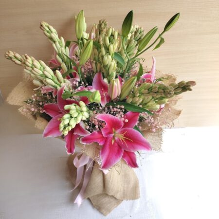 Fresh lily and rose bouquet wrapped in burlap, featuring pink lilies, white roses, and lush green buds.