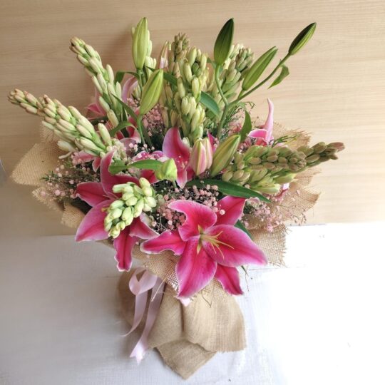 Fresh lily and rose bouquet wrapped in burlap, featuring pink lilies, white roses, and lush green buds.