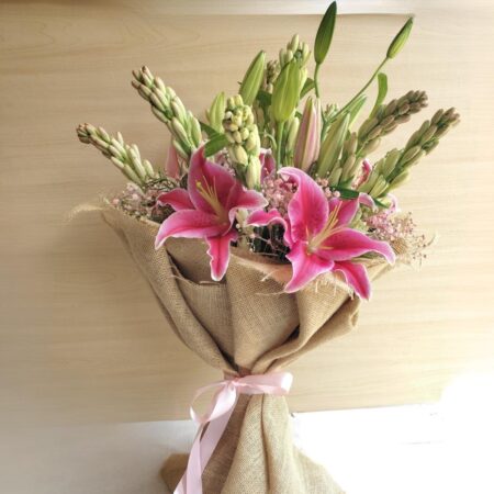 Fresh lily and rose bouquet wrapped in burlap, featuring pink lilies, white roses, and lush green buds.