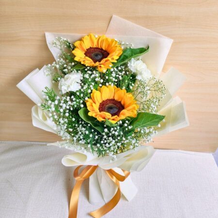 A cheerful sunflower bouquet paired with white carnations and baby’s breath, elegantly wrapped in cream paper with a golden ribbon — available for same day flower delivery in Bangalore.