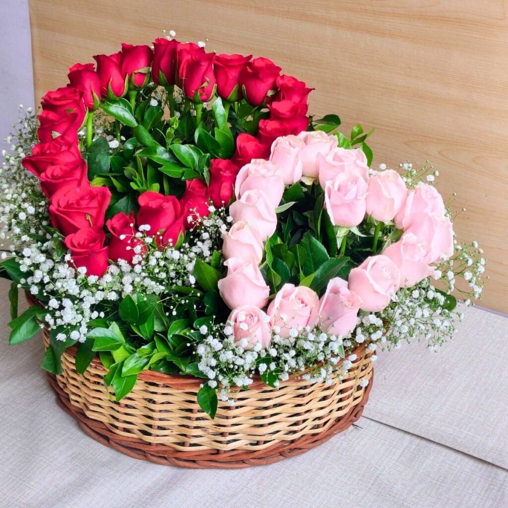 Heart-shaped red and pink rose arrangement in a basket with baby’s breath and greenery.