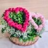Heart-shaped red and pink rose arrangement in a basket with baby’s breath and greenery.