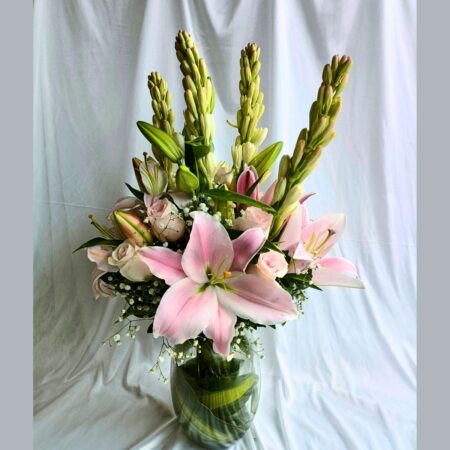 A tall floral arrangement in a glass vase featuring soft pink lilies, pale pink roses, and white buds with lush green leaves — perfect for same day flower delivery in Bangalore.