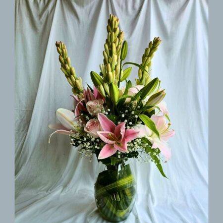 A tall floral arrangement in a glass vase featuring soft pink lilies, pale pink roses, and white buds with lush green leaves — perfect for same day flower delivery in Bangalore.