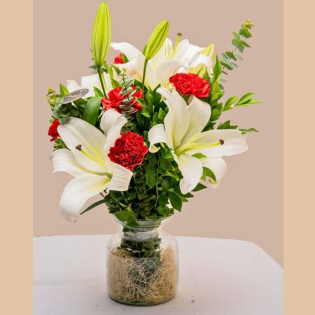 A glass vase arrangement of white lilies and red carnations with lush green foliage — ideal for same day flower delivery in Bangalore.