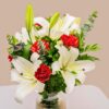A glass vase arrangement of white lilies and red carnations with lush green foliage — ideal for same day flower delivery in Bangalore.
