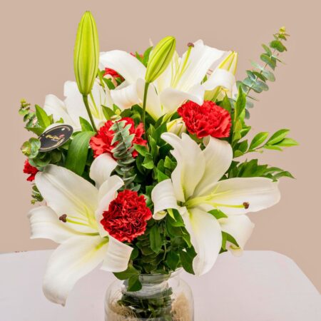 A glass vase arrangement of white lilies and red carnations with lush green foliage — ideal for same day flower delivery in Bangalore.