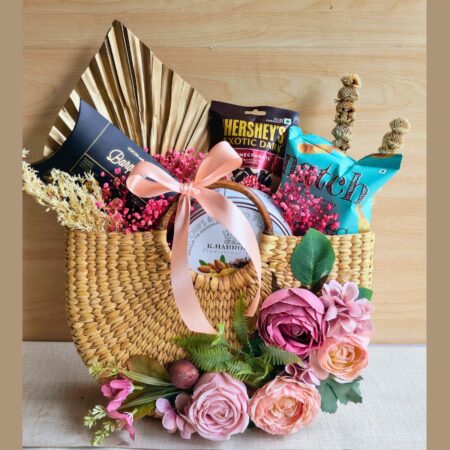 Luxury woven gift hamper with chocolates, snacks, and pink artificial flowers from FreshKnots Bangalore.