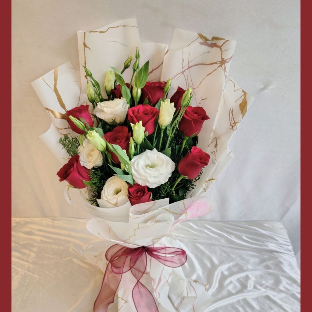 Red and white fresh flower bouquet of roses and eustoma (exotic flower) wrapped in marble paper with satin ribbon.