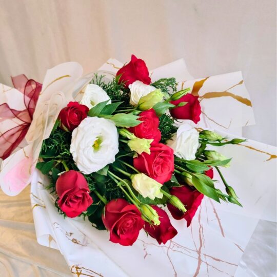 Red and white fresh flower bouquet of roses and eustoma (exotic flower) wrapped in marble paper with satin ribbon.