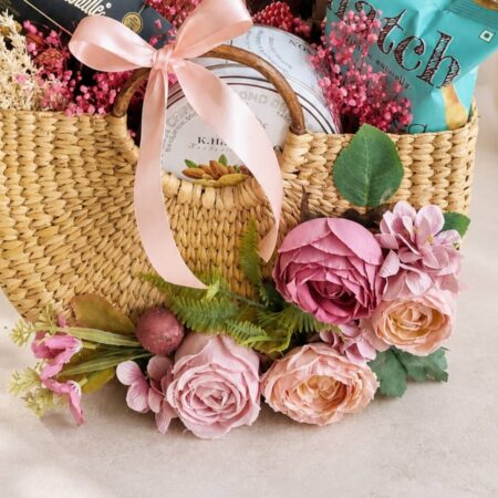 Luxury woven gift hamper with chocolates, snacks, and pink artificial flowers from FreshKnots Bangalore.