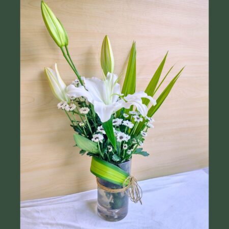 Elegant white lily flower arrangement in a glass vase with greenery and natural twine.