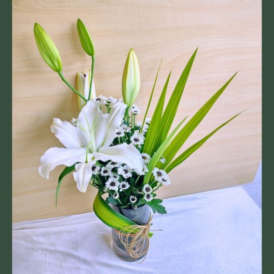 Elegant white lily flower arrangement in a glass vase with greenery and natural twine.