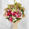 Fresh lily and rose bouquet wrapped in burlap, featuring pink lilies, white roses, and lush green buds.