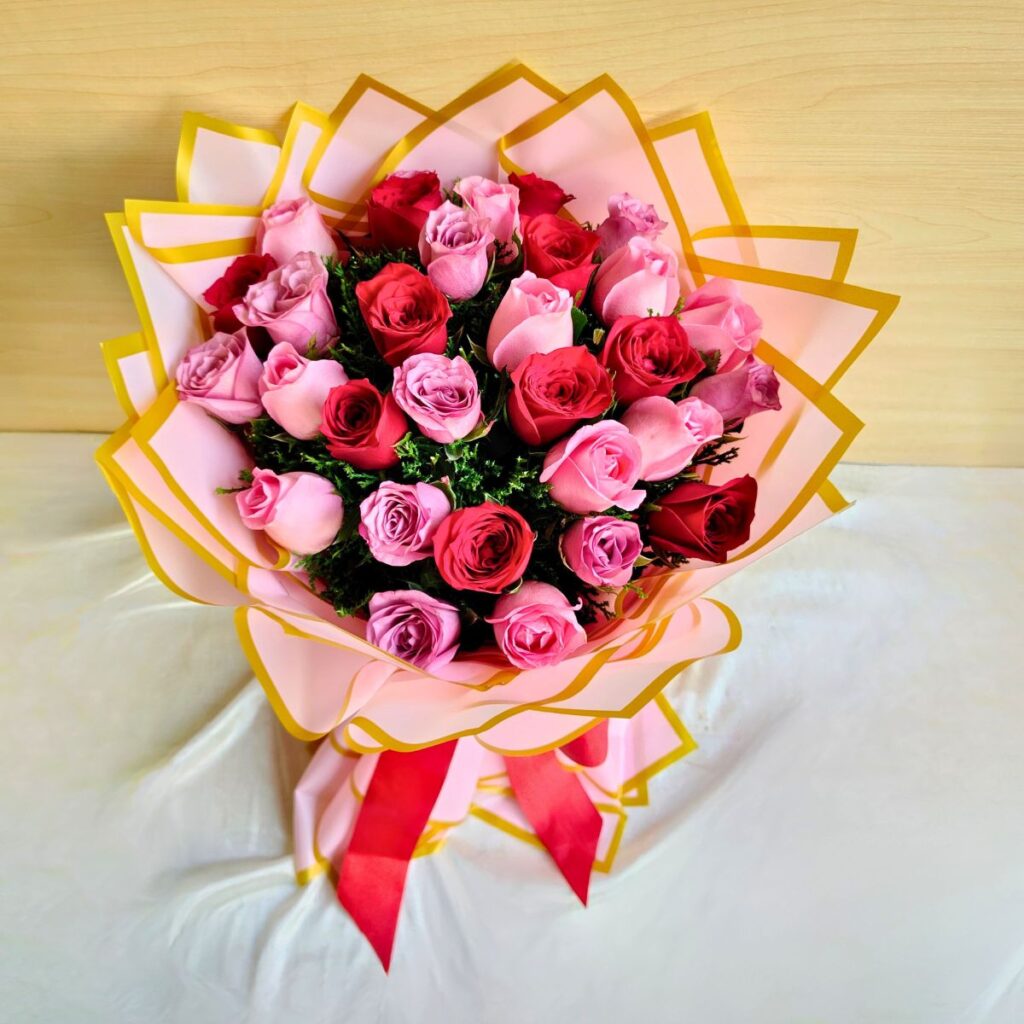 Handcrafted bouquet of red and pink roses wrapped in pink and gold paper with satin ribbon.