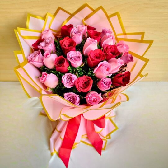 Handcrafted bouquet of red and pink roses wrapped in pink and gold paper with satin ribbon.