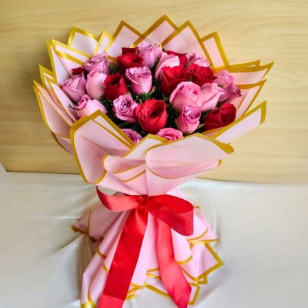 Handcrafted bouquet of red and pink roses wrapped in pink and gold paper with satin ribbon.