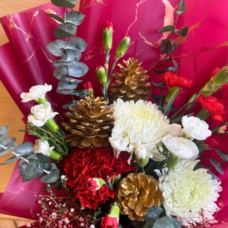 “Christmas flower bouquet with red and white flowers, gold pine cones, and winter greens, wrapped in burgundy and gold paper – FreshKnots Bangalore.”