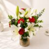 A glass vase arrangement of white lilies and red carnations with lush green foliage - ideal for same day flower delivery in Bangalore.