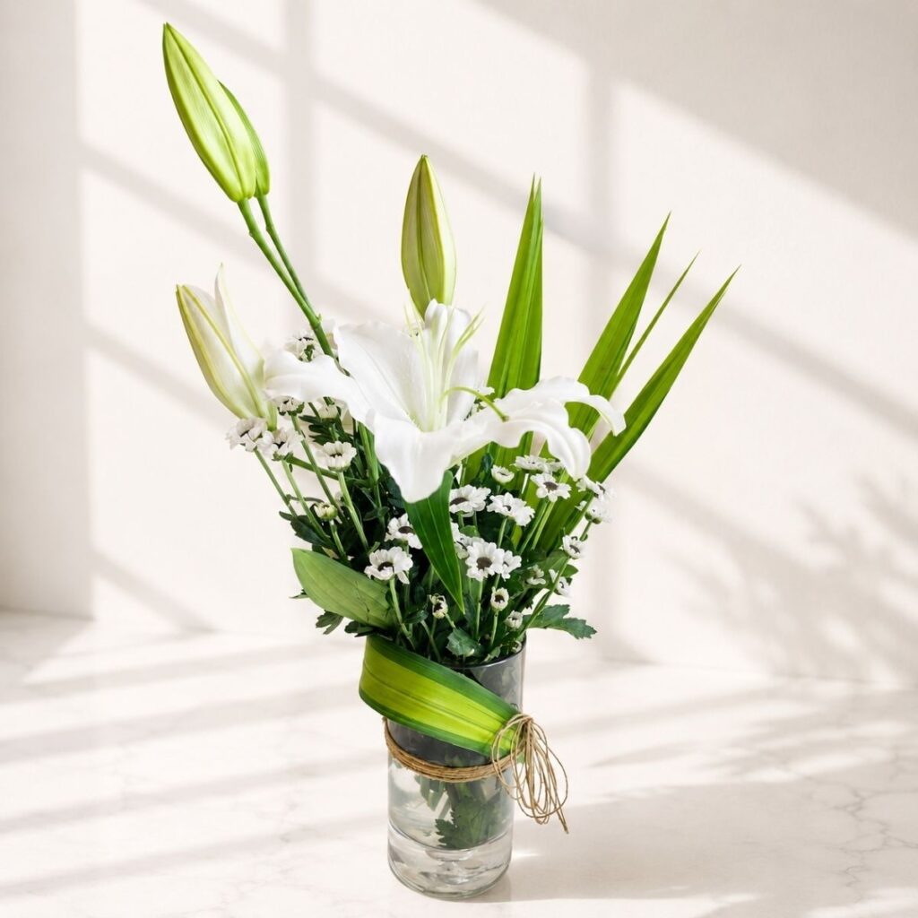 Elegant white lily flower arrangement in a glass vase with greenery and natural twine.