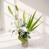 Elegant white lily flower arrangement in a glass vase with greenery and natural twine.