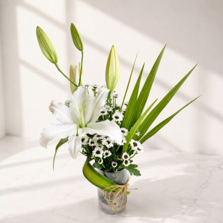 Elegant white lily flower arrangement in a glass vase with greenery and natural twine.