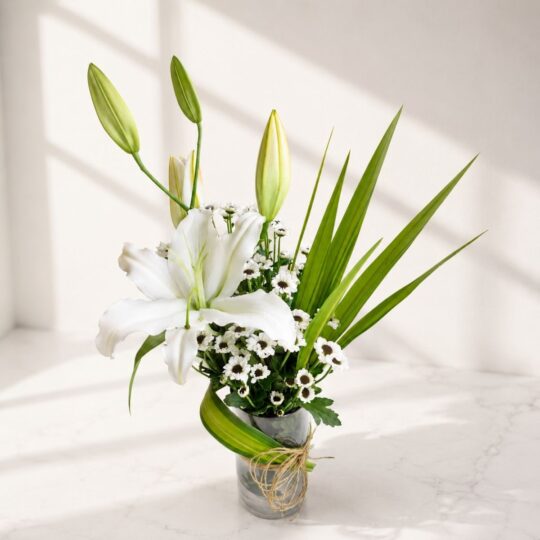 Elegant white lily flower arrangement in a glass vase with greenery and natural twine.