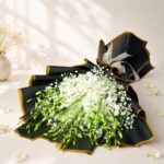 White orchid bouquet lying flat, black and gold wrap Bangalore