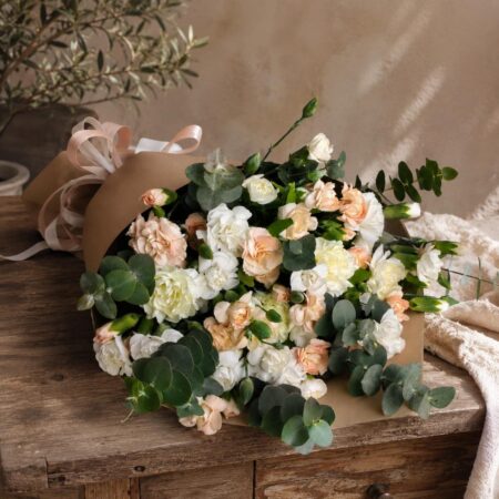 Peach and white spray carnations with eucalyptus in kraft wrap laid on a wooden table