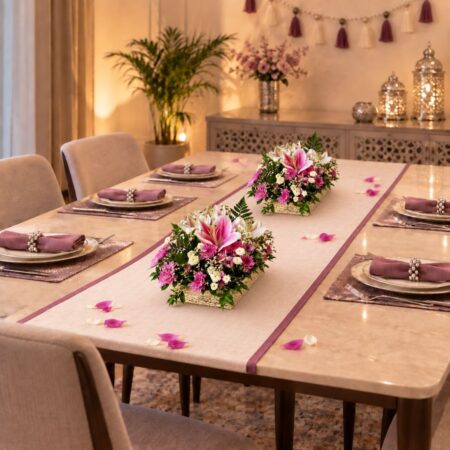 Two lily and chrysanthemum centrepieces on a Diwali dining table with pink napkins and lanterns
