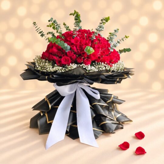 Large red rose hand bouquet in layered black and gold wrap with a white satin ribbon, side angle