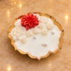 Close-up of a scented candle in a gold metal urli decorated with a red wax flower, white wax flowers and pearls. Urli Diya.