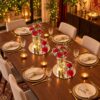 Two red carnation and baby's breath centrepieces with candles on mirror bases along a dining table