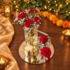Glass jar of red carnations and baby's breath lit with fairy lights beside a votive candle on a mirror, angled view