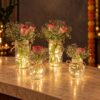 Four glass jars of roses and baby's breath lit from inside with cork fairy lights, front view