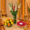 Tall tuberose and red gladiolus glass vase with a marigold matki vase and rose petal urli, angled view