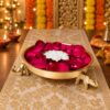 Metal urli filled with fresh red rose petals and a metal urli candle at the centre, close-up